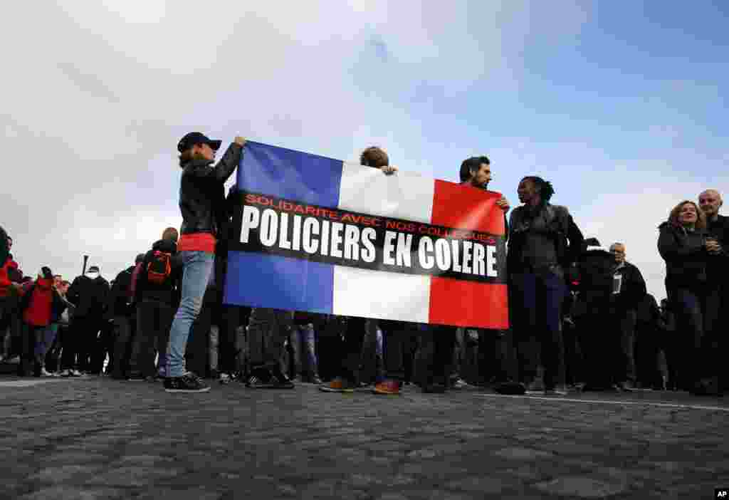 Polisi memegang bendera Perancis bertuliskan "Polisi yang Marah" dalam demonstrasi di depan Majelis Nasional di Paris (26/10). (AP/Christophe Ena)