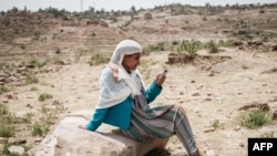 A woman attempts to reach mobile phone signal after most of an area is in blackout in Samre, southwest of Mekele in Tigray region, Ethiopia, on June 20, 2021. (Yasuyoshi Chiba/AFP)