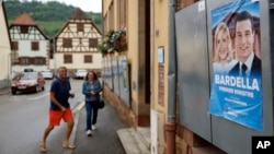 Glasači stižu na biračko mjesto u Soultz-Les-Bainsu, istočna Francuska, 30. juna 2024. Poster s francuskim liderima krajnje desnice Marine Le Pen i Jordanom Bardellom vidi se na desnoj strani.