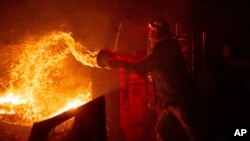 Francis Lopez douses flames with a bucket of water as a wildfire called the Highland Fire burns through his property in Aguanga, Calif., Oct. 30, 2023. 