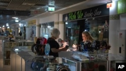 Seorang penjual menyorotkan senter saat dia menunjukkan barang kepada pelanggan saat listrik padam di Kyiv, 19 Juni 2024. Serangan rudal besar-besaran yang dilakukan Rusia terhadap fasilitas energi Ukraina telah mengakibatkan pembatasan pasokan listrik.