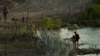 A Texas state trooper watches as young migrants walk along concertina wire on the banks of the Rio Grande as they try to enter the U.S. from Mexico in Eagle Pass, Texas, July 6, 2023. 