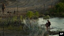 A Texas state trooper watches as young migrants walk along concertina wire on the banks of the Rio Grande as they try to enter the U.S. from Mexico in Eagle Pass, Texas, July 6, 2023. 