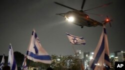Moun flote drapo Izrayelyen nan moman yon elikopte kap transpote otaj Hamas lage nan Gaza rive nan sant medikal pou timoun Schneider la nan Petah tikva, Izrayel, Dimanch 26 Nov. 2023.