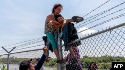 Seorang perempuan migran membantu putranya memanjat pagar kawat berduri setelah melintasi sungai Rio Grande dari Meksiko untuk memasuki kota Eagle Pass, Texas di Amerika Serikat (foto: ilustrasi). 