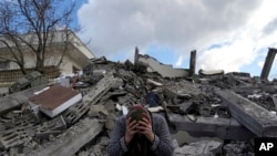 FILE - A woman sits on the rubble as emergency rescue teams search for people under the remains of destroyed buildings in Nurdagi town on the outskirts of Osmaniye city southern Turkey, on Feb. 7, 2023.