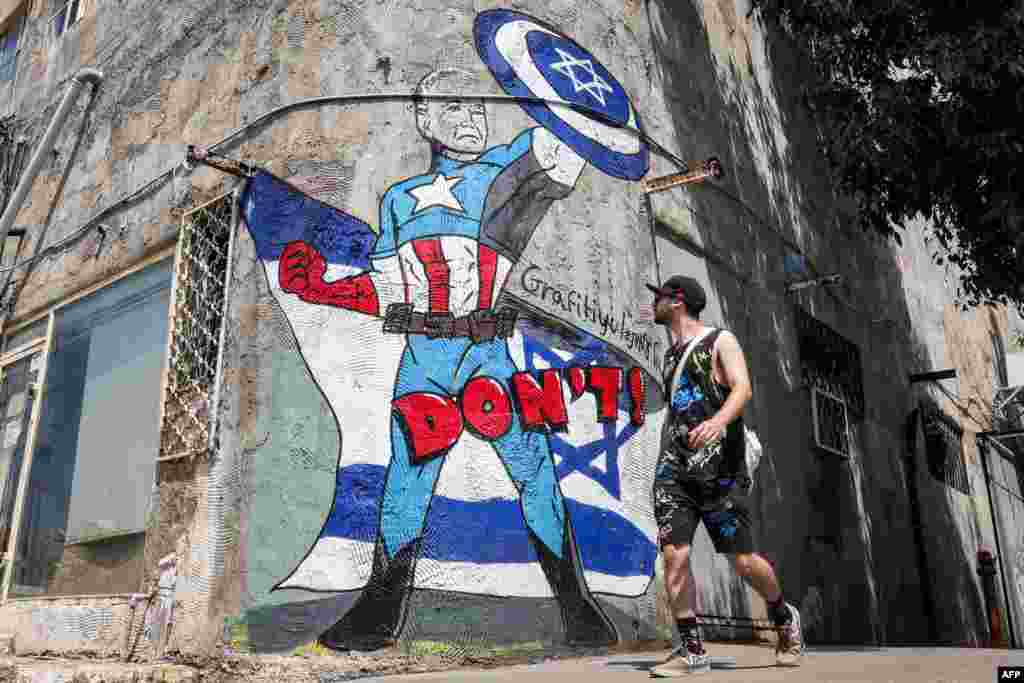 A man walks past a mural drawn by the "Grafitiyul" graffiti art group depicting U.S. President Joe Biden dressed as the Marvel comics character "Captain America" standing before an Israeli flag and holding up his shield depicting the Star of David symbol, along a street in Tel Aviv.