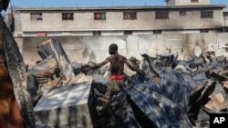Seorang warga tampak mencari benda yang masih bisa diselamatkan dari sebuah toko peralatan mobil yang dibakar dalam kekerasan geng di Port-au-Prince, Haiti, pada 25 Maret 2024. (Foto: AP/Odelyn Joseph) 