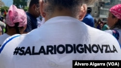 Una trabajadora muestra un eslogan por mejores condiciones laborales grabado en su camiseta, durante una protesta celebrada el 1 de mayo de 2024 en Caracas.
