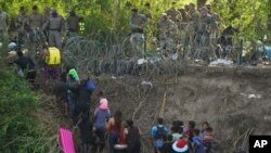 Texas state police finish placing barbed-wire as migrants walk up the bank of the Rio Grande river, seen from Matamoros, Mexico, May 10, 2023. 