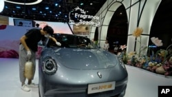 Seorang karyawan sedang membersihkan mobil listrik Ora di sebuah pameran di Shanghai, China, 18 April 2023. (Foto: Ng Han Guan/AP Photo)