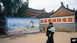資料照 - 這張美聯社的照片攝於1972年4月台灣的金門島。一位長者抱著他的孫子走過一幅“整軍經武反攻大陸“的宣傳壁畫。