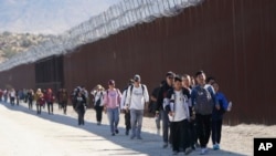 Un grupo de personas, entre ellas muchas de China, caminan a lo largo del muro después de cruzar la frontera con México para buscar asilo, cerca de Jacumba, California, el 24 de octubre de 2023.