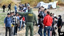 A U.S. Border Patrol agent directs asylum-seekers waiting between the double fence along the U.S.-Mexico border near Tijuana, Mexico, May 8, 2023, in San Diego, California. The migrants wait between the fences to be processed by U.S. Border Patrol agents.