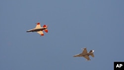 ເຮື​ບິນ​ລົບກອງ​ທັບ​ອາ​ກາດ F-16 ທີ່​ໃຊ້​ປັນ​ຍາ​ປະ​ດິດ​ບັນ​ຊາ, ຊ້າຍ, ບິນ​ຢູ່​ທາງ​ຂ້າງ​ເຮືອ​ບິນລົບ F-16 ທີ່​ສົມ​ມຸດ​ວ່າ​ເປັນ​ສັດ​ຕູ ພະ​ຍາ​ຍາມ​ທີ່​ຈະ​ບັງ​ຄັບ​ຄູ່​ຕໍ່​ສູ້​ຂອງ​ມັນ​ໄປ​ຈຸດ​ທີ່​ມີ​ຄວາມ​ສ່ຽງ, ຢູ່​ເທິງ​ຖານ​ທັບ​ອາ​ກາດ ເອັດ​ເຫວີດ​ສ໌, ລັດ​ຄາ​ລິ​ຟໍ​ເນຍ, 2 ພຶດ​ສະ​ພາ 2024.