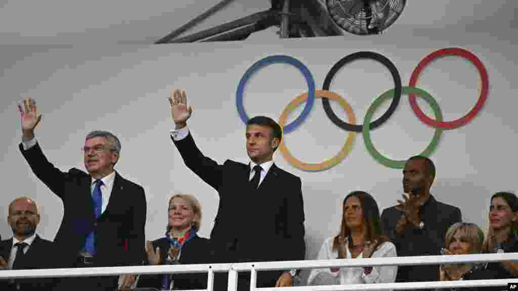 Presiden Prancis Emmanuel Macron, tengah, dan Presiden Komite Olimpiade Internasional (IOC) Thomas Bach, kiri, melambaikan tangan saat mereka tiba untuk menghadiri upacara pembukaan Olimpiade Musim Panas 2024 di Paris, 26 Juli 2024. (Foto: Loic Venance/Pool Photo via AP)