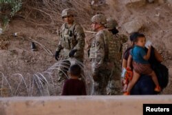 Migrants stand near the Rio Bravo river after crossing the border, to request asylum in the United States, as members of the Texas Army National Guard extended razor wire, as seen from Ciudad Juarez, Mexico, May 13, 2023.