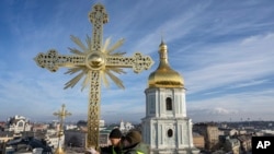 Dos hombres instalan una cruz restaurada en la cúpula de la Catedral de Santa Sofía en Kiev, Ucrania, el 21 de diciembre de 2023.