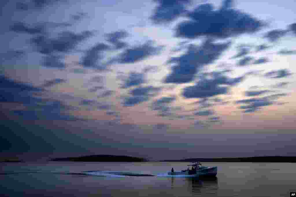 A lobster fishing boat motors out to sea under the dawn sky on Casco Bay in South Portland, Maine.