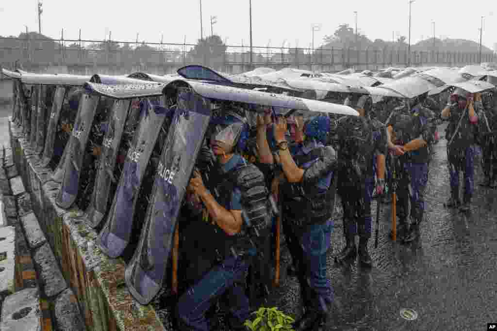 Police personnel use shields as cover during rainfall along the main road leading to the House of Representatives ahead of the third State of the Nation Address by Philippine President Ferdinand Marcos Jr. in Quezon City.