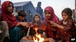 Anak-anak pengungsi Afghanistan menghangatkan diri di api unggun di sebuah kamp dekat perbatasan Pakistan di Torkham, Afghanistan, setelah mereka dideportasi dari Pakistan.