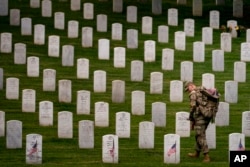 ARCHIVO - Un miembro del 3.er Regimiento de Infantería de EEUU coloca banderas frente a cada lápida para "Flags-In" en el Cementerio Nacional de Arlington en Arlington, el 25 de mayo de 2023, para honrar a los héroes militares caídos de la nación antes del Día de los Caídos.