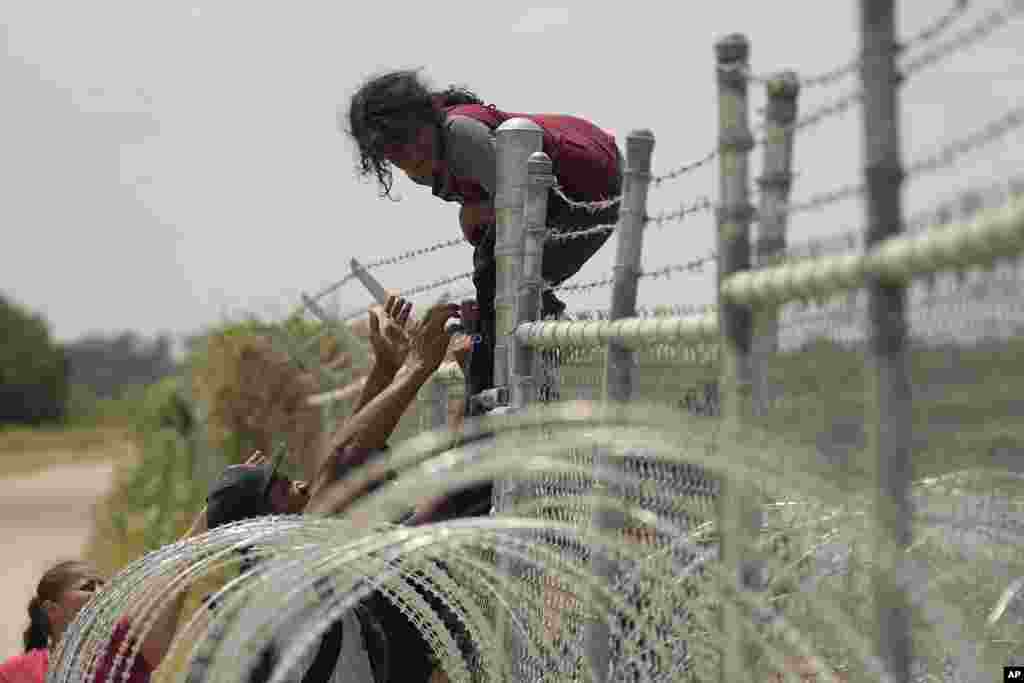 Migrants who crossed the Rio Grande from Mexico into the U.S. climb a fence with barbed wire and concertina wire, Aug. 21, 2023, in Eagle Pass, Texas.