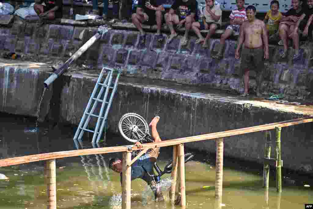 A child falls during a bicycle balance competition over a plank on a river, part of community festivities ahead of the 79th anniversary of Indonesia's Independence Day, in Surabaya.
