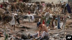 A man washes his clothes in a stream near debris left over after flooding devastated the village of Nanxinfang village on the outskirts of Beijing, Aug. 4, 2023. (AP/Ng Han Guan)