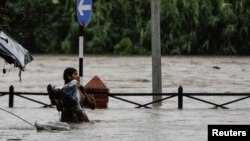 A woman carrying her belongings wades through a flooded road along the bank of overflowing Bagmati River following heavy rains in Kathmandu, Nepal, July 6, 2024. 
