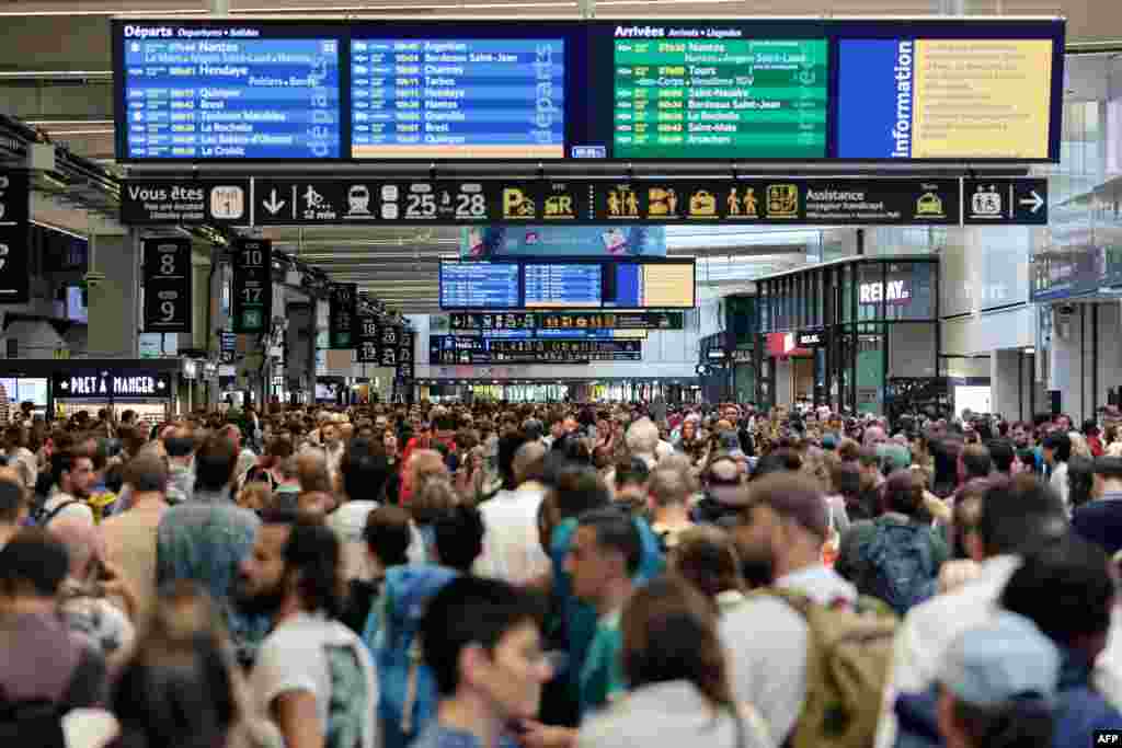 Passengers gather around departure and arrival boards at the Gare Montparnasse train station in Paris as France's high-speed rail network was hit by malicious acts disrupting the transport system hours before the opening ceremony of the Paris 2024 Olympic Games.