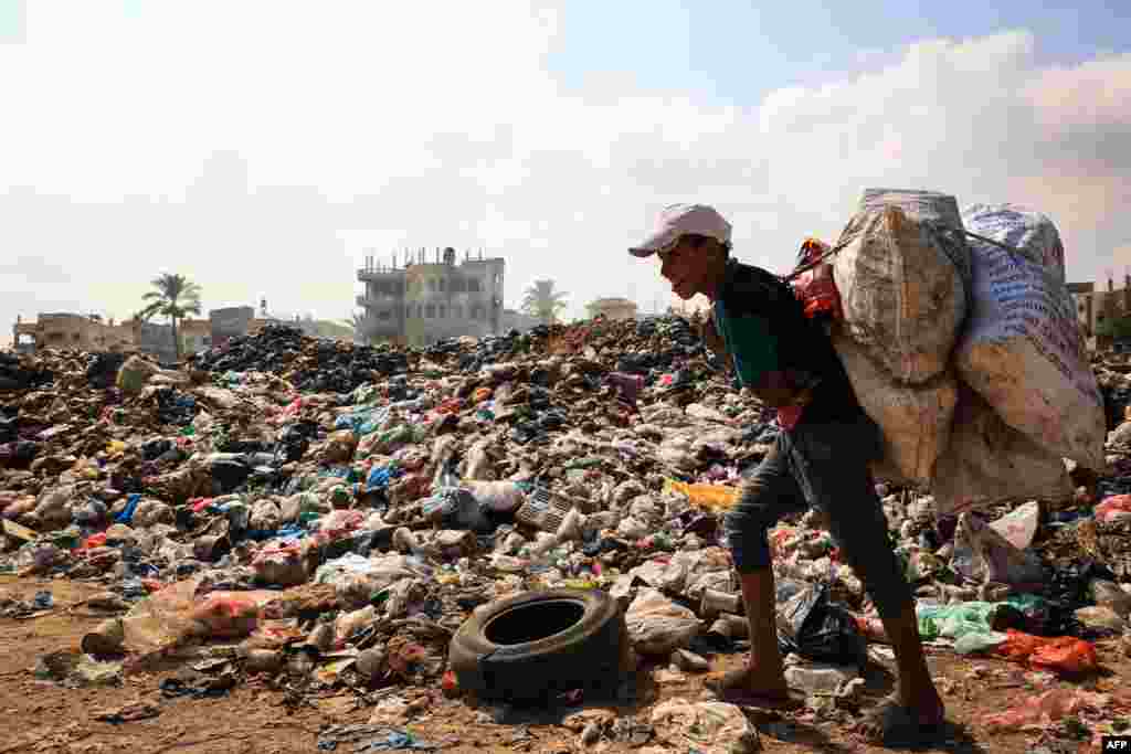 A Palestinian youth carrying sacks of salvageable items walks past piles of waste as garbage collection and any other municipality services come to a halt due to the Israeli bombardment of the Gaza Strip, at the al-Maghazi Palestinian refugee camp, in the central Gaza Strip. 
