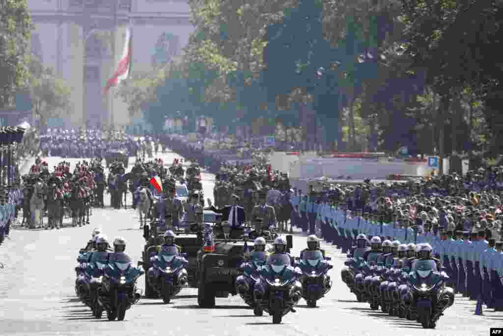 France's President Emmanuel Macron (centre L) waves in the command car during the Bastille Day military parade on the Avenue Foch, with the Arc de Triomphe in the background in Paris.