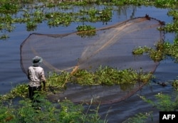 FILE - A man throws a fishing net into a lake in Kandal province, near Phnom Penh, Cambodia, Sept. 24, 2023. (Photo by TANG CHHIN Sothy / AFP)