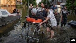 Voluntarios transportan a una mujer en una camilla para ser evacuada de un barrio inundado en Jersón, Ucrania, el 9 de junio de 2023.