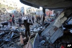 Warga Palestina berdiri di dekat sebuah bangunan yang hancur akibat pemboman Israel di Rafah, Jalur Gaza, 24 November 2023. (Foto: AP)