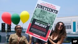 Dos personas sostienen un cartel desde su automóvil durante un desfile para conmemorar el 19 de junio de 2021, en Inglewood, California.