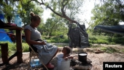 Pencari suaka asal Venzuela, Alejandra Pena, 34, memandikan anaknya Natanael, 1, di sebuah ember plastik di samping tenda mereka di kamp pengungsi di Matamoros, Meksiko, pada 20 Juni 2023. (Foto: Reuters/Daniel Becerril)