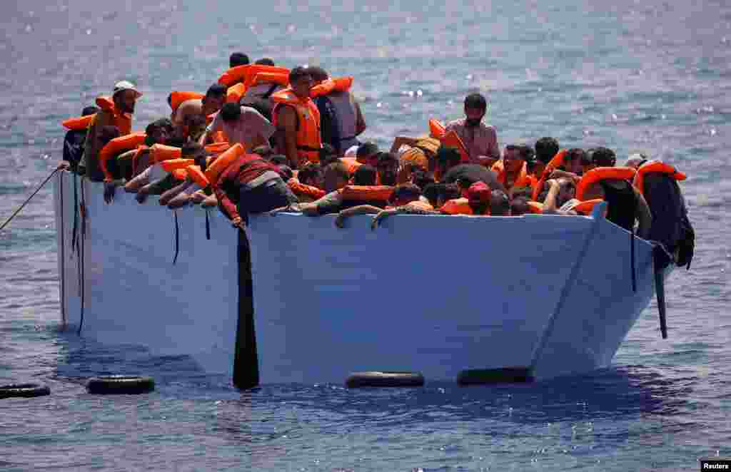 Migrants stands on a wooden boat near NGO Open Arms rescue boat "Astral" in international waters south of Lampedusa, in the Mediterranean Sea.
