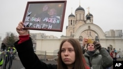 Seorang perempuan memegang potret Alexey Navalny dan istrinya, Yulia, di luar gereja tempat pemakamannya berlangsung, di Moskow, Rusia, 1 Maret 024. (Foto: AP Photo)