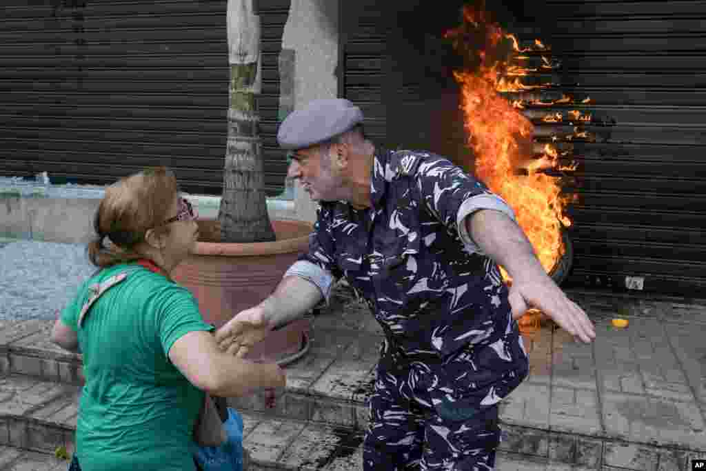 A police officer speaks with a protesting depositor as they stand in front of burning tires set on fire in front of a branch of Emirates Lebanese Bank in Dawra, a suburb north-east of Beirut, Lebanon. Depositors demand their trapped savings deposits as they struggle from an economic crisis.