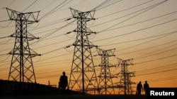 FILE - Locals walk past electricity pylons in Soweto, South Africa, July 3, 2022.