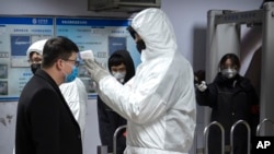 Mfanyakazi wa afya akipima joto la mwili wa msafiri aliyekuwa anaingia katika stesheni ya treni za mjini jijini Beijing, Jumapili, Jan. 26, 2020. 