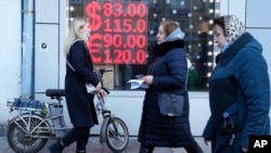 FILE - People walk past a currency exchange office screen displaying the exchange rates of U.S. Dollar and Euro to Russian Rubles in Moscow's downtown, Feb. 28, 2022.