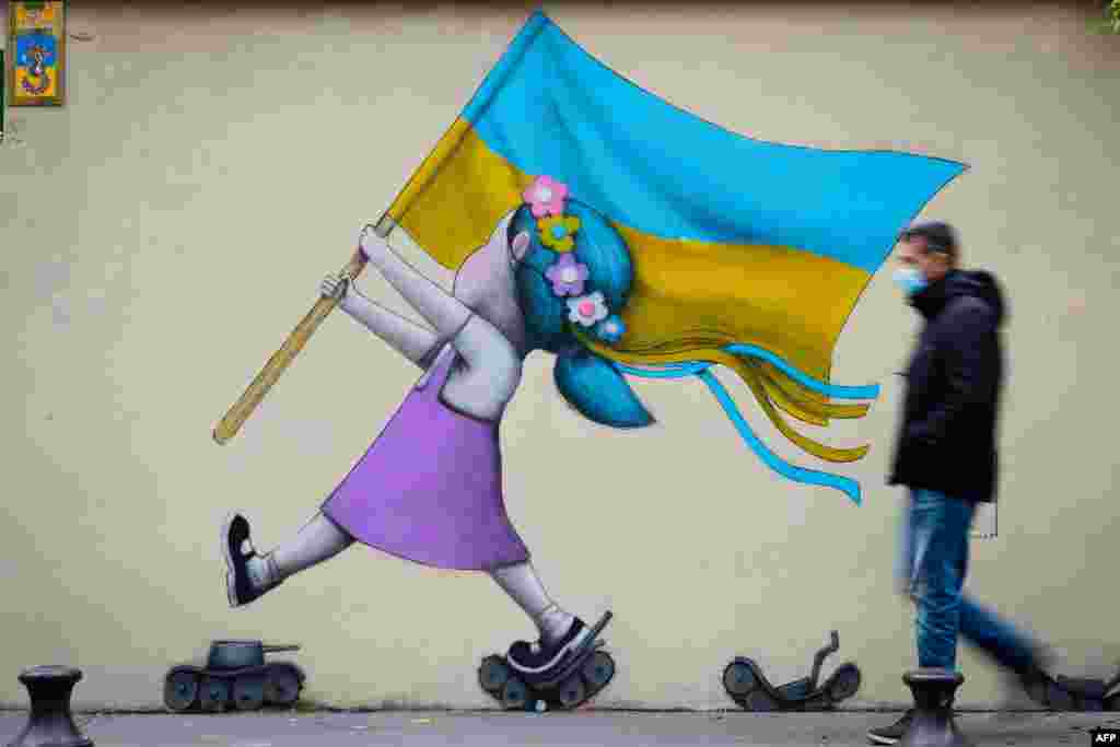 A bystander walks past a fresco by street artist Seth depicting a girl with a Ukrainian flag walking on tanks in Paris, France.