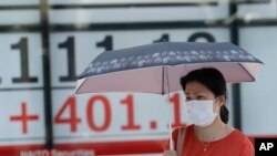 A woman wearing a face mask walks by an electronic stock board of a securities firm in Tokyo, Aug. 3, 2020.