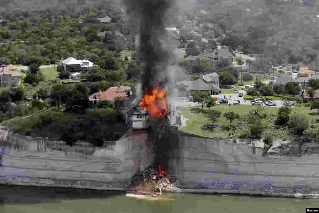 Smoke rises from a house deliberately set on fire, days after part of the ground it was resting on collapsed into Lake Whitney, Texas. Building crews set fire to the luxury lake house left dangling about 75 feet (23 meters) on a decaying cliff that has been giving way underneath the structure.