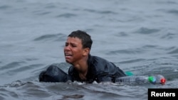 Achraf, de 16 años, llora mientras nada usando botellas de plástico como flotadores, cerca de la valla entre la frontera entre España y Marruecos, después de que miles de inmigrantes cruzaron la frontera nadando, en Ceuta, España, el 19 de mayo de 2021.