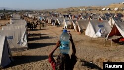FILE - A girl carries a bottle of water she filled from nearby standing floodwaters at a camp for those displaced by recent flooding, in Sehwan, Pakistan, Sept. 30, 2022. 
