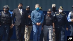 Former Honduran President Juan Orlando Hernandez, center, is taken in handcuffs to a waiting aircraft as he is extradited to the United States, at an Air Force base in Tegucigalpa, Honduras, April 21, 2022.